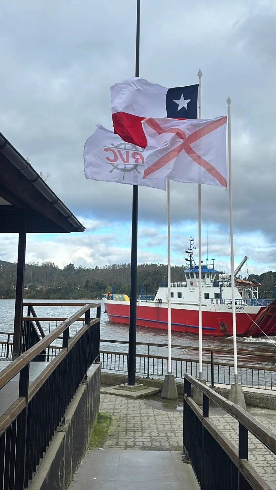 Banderas de Chile y de RVC en el muelle, con la Cullamó navegando detrás
