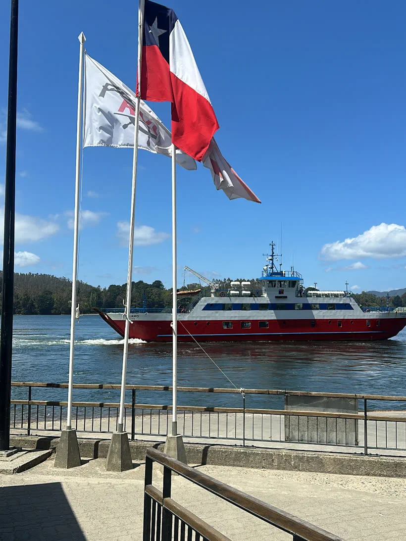 Muelle de embarque con las banderas de Chile y de RVC, y una barcaza navegando al fondo